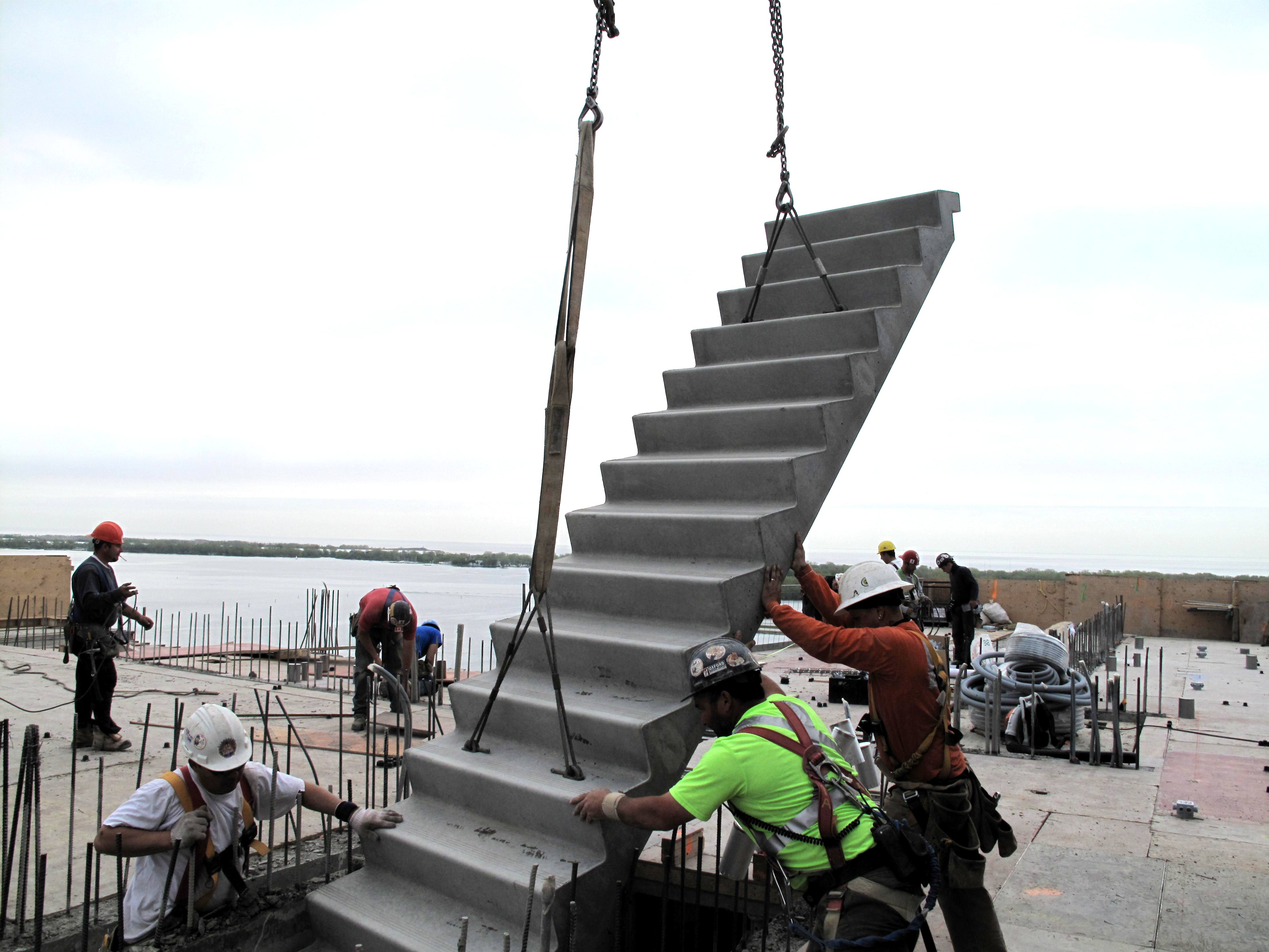 Construction Workers Guiding Precast Concrete Stairs That Are Being Crane Dropped Into Proper Position